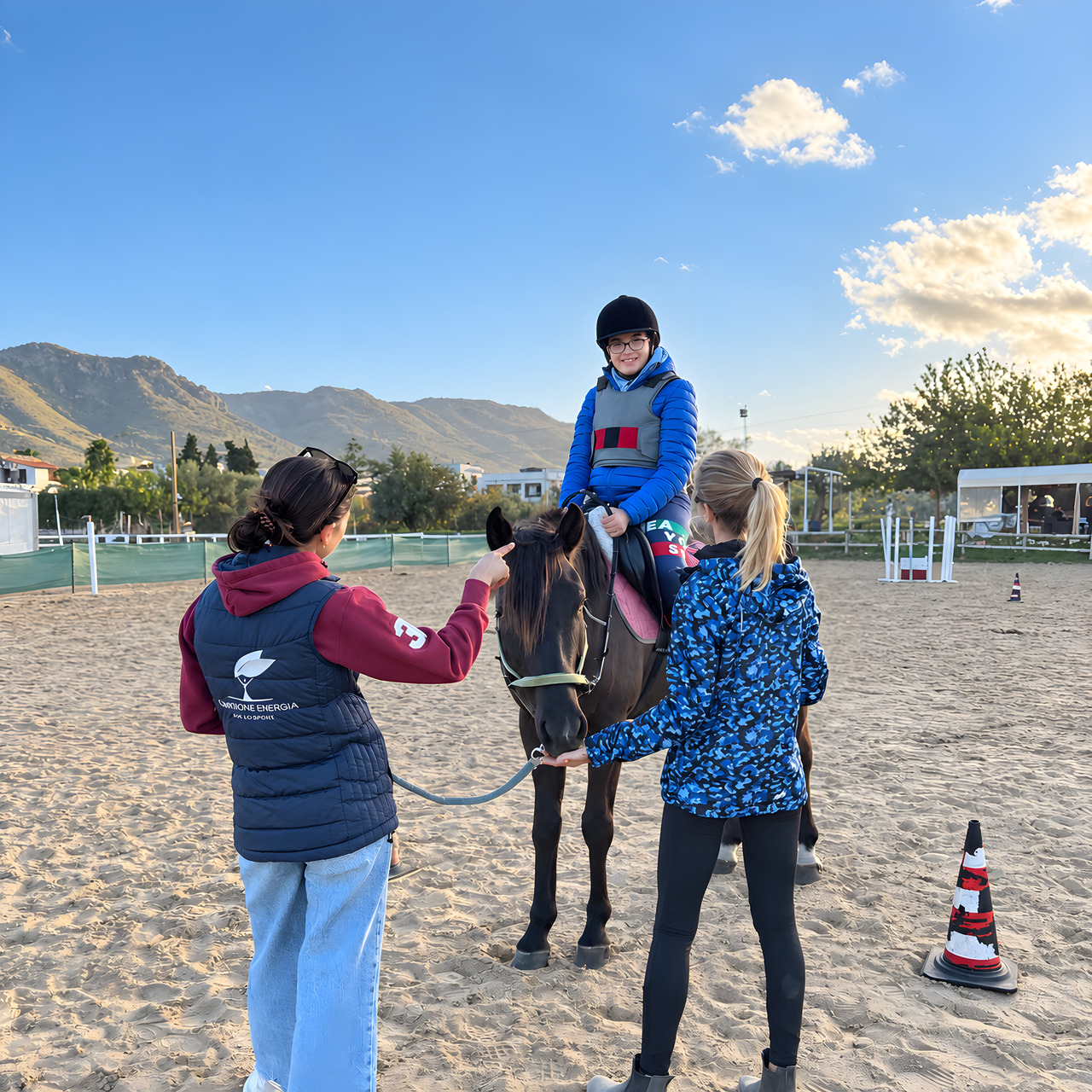 Un bambino a cavallo nel campo in sabbia, accompagnato a mano da due operatrici
