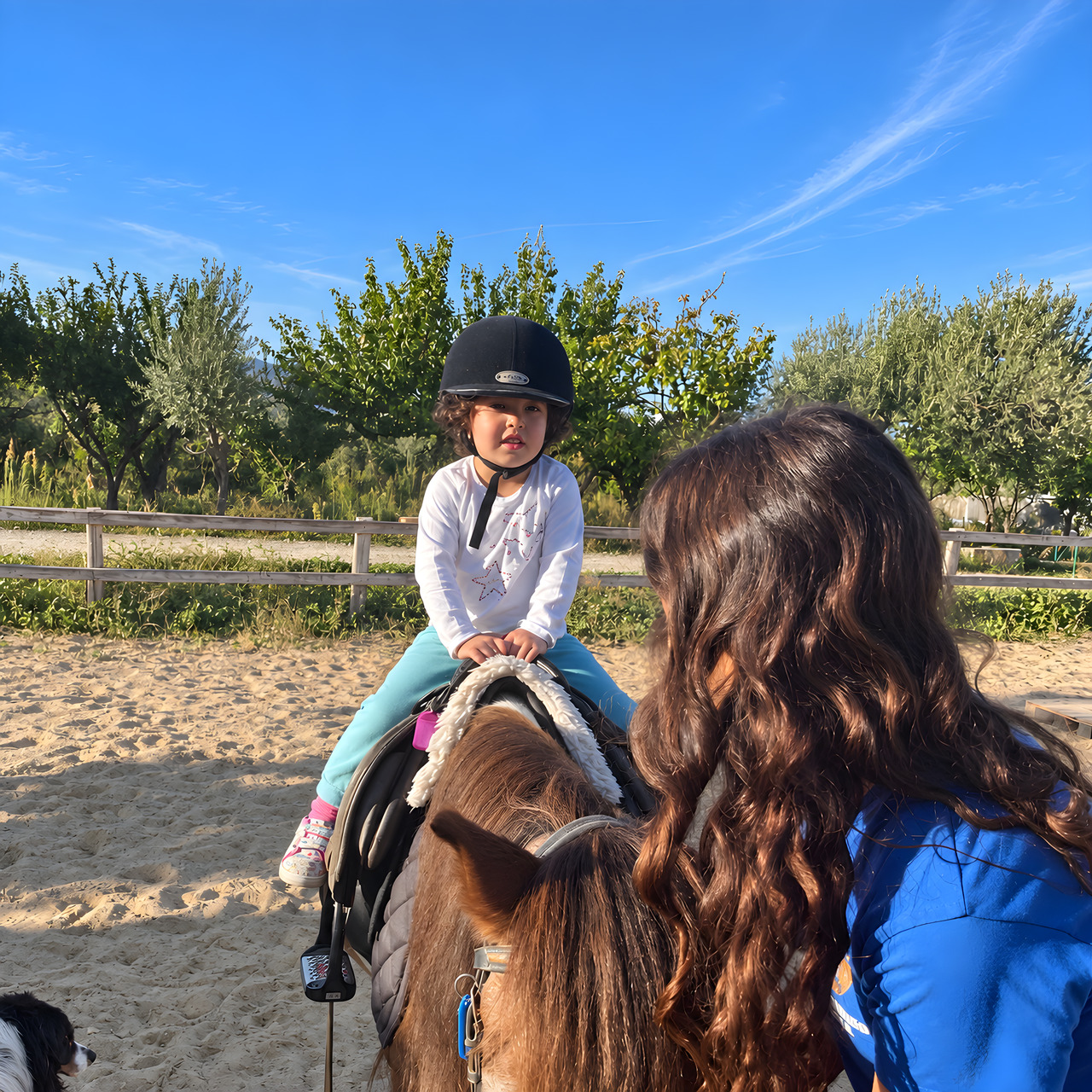 Una ragazza a cavallo nel campo, accompagnata a mano da un’operatrice